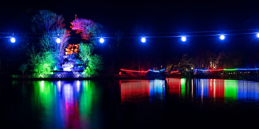 Two ladies hold hands in front of illuminated boats at Scarborough Harbour
